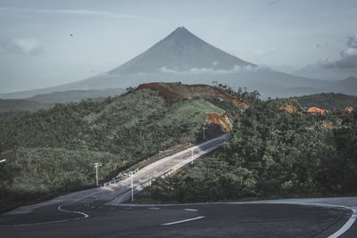 Empty road leading towards mountain against sky