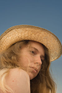 Low angle view of thoughtful young woman wearing hat against clear sky