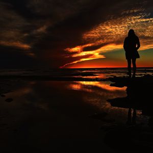 Silhouette of people standing on beach against cloudy sky