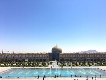 People in front of historical building against clear blue sky