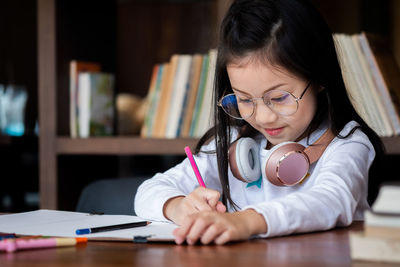 Close-up of girl writing on book at desk