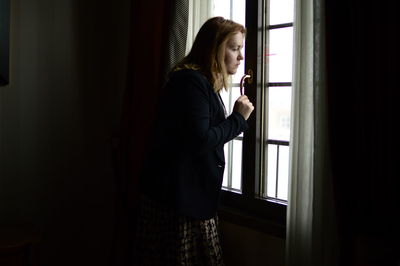 Side view of woman looking through window at home