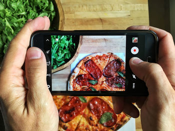 Cropped image of hand photographing pizza at table