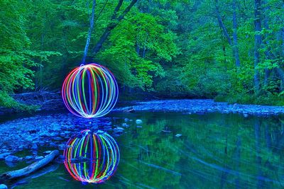 Multi colored light trails over lake in forest