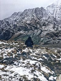 Rear view of man standing on snowcapped mountain against sky