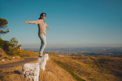 Side view of happy mid adult woman with arms outstretched standing on mountain against blue sky