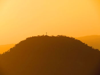 Low angle view of cross on mountain against clear orange sky during sunset