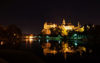 Illuminated buildings by river against sky at night