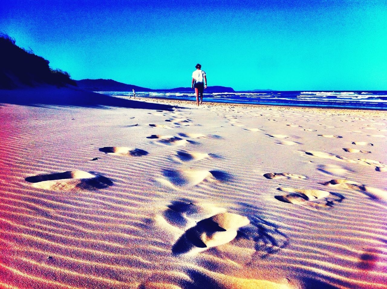 sand, beach, clear sky, blue, leisure activity, full length, shore, sunlight, lifestyles, vacations, sea, tranquility, tranquil scene, summer, relaxation, copy space, nature, footprint