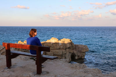 Man sitting on bench looking at sea against sky