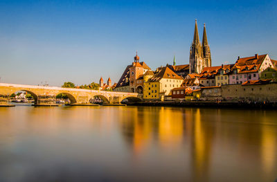 Arch bridge over river amidst buildings against clear sky