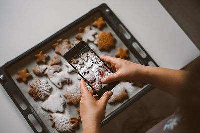 Woman takes photo on smartphone christmas gingerbread sprinkled with powdered sugar.