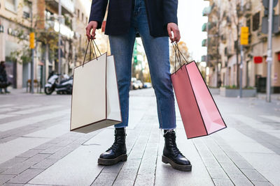 Crop unrecognizable female buyer standing in street with paper bags after shopping in city