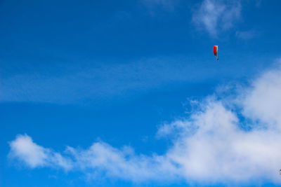 Low angle view of people paragliding against blue sky