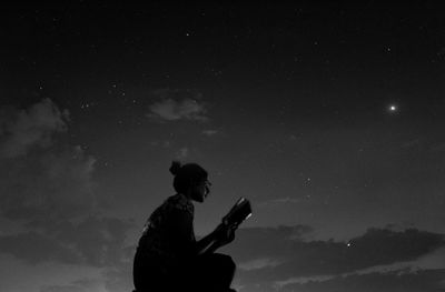 Silhouette of man using smart phone against sky at night