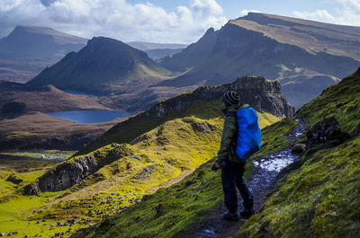 Side view of man with backpack standing on mountain against sky