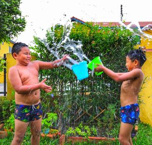 Shirtless brothers pouring water on each other while standing in yard