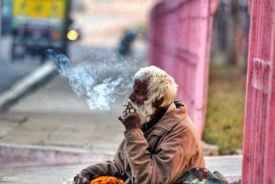 Senior man smoking while sitting on footpath