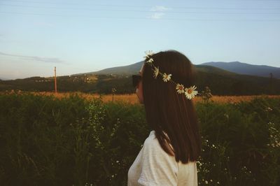 Side view of woman wearing daisy flowers tiara while standing on field against sky