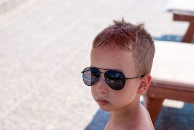 Close-up portrait of shirtless boy wearing sunglasses at poolside