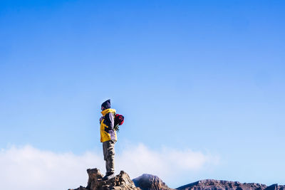 Low angle view of man standing on rock against blue sky