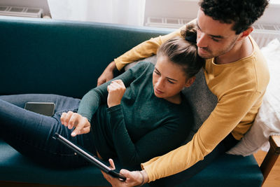 Rear view of man and woman using mobile phone while sitting on sofa