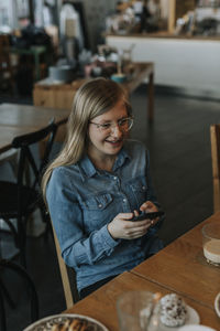 Young woman using mobile phone while sitting on table