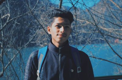 Portrait of young man standing by bare tree