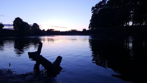 Reflection of silhouette trees on water against sky