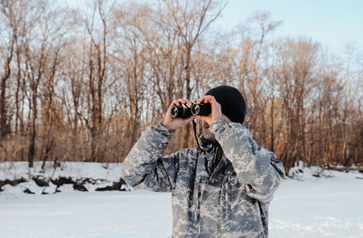 Man photographing woman standing on snow covered bare trees