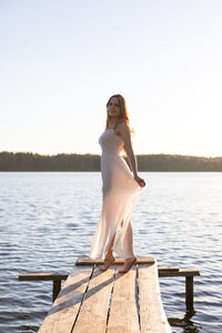 Beautiful russian girl dressed in a white dress, walking along a wooden pier on the bank of a river.