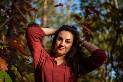 Outdoor close-up portrait of young woman in red dress looking at camera. autumn leafes in background