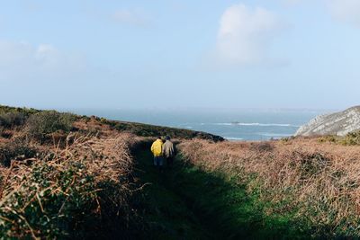 Rear view of men walking on field against sky