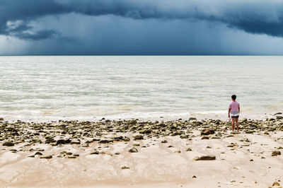 Rear view of woman walking on beach against sky