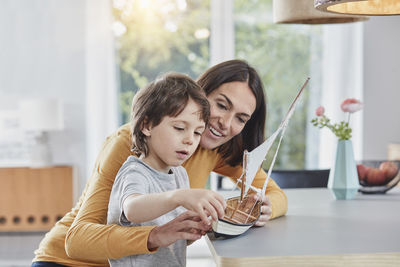 Happy mother and son playing with model boat at home