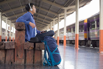 Side view of man listening music on headphones while sitting at railroad station platform
