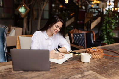 Young caucasian business woman with long brunette hair working on laptop in cafe. 