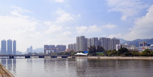 Buildings by river against sky in city