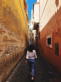 Rear view of woman walking on footpath amidst buildings