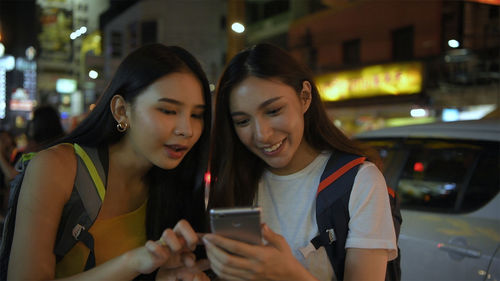 Smiling young woman using phone on city at night