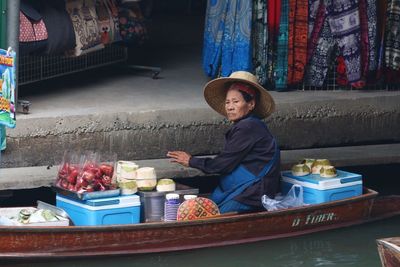 Full length of boy sitting at market stall for sale