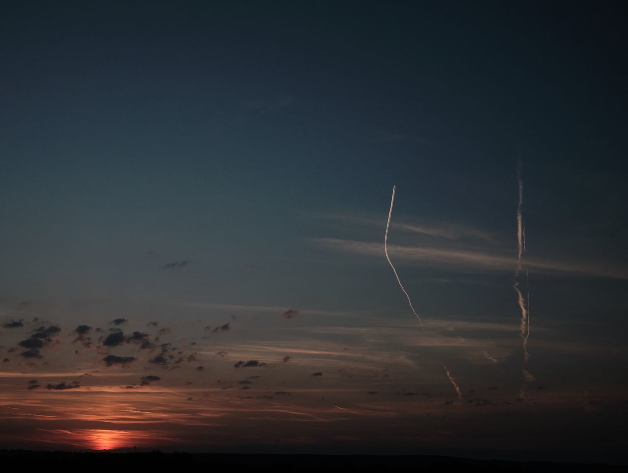 LOW ANGLE VIEW OF VAPOR TRAILS IN SKY AT SUNSET