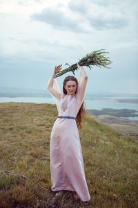 Woman stands on a mountain cliff in a pink long dress in summer