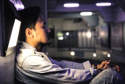 Side view portrait of young man sitting in illuminated room