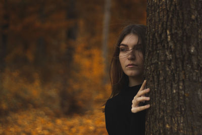 Beautiful woman standing by tree trunk in forest