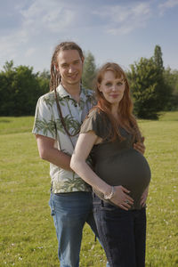 Portrait of pregnant woman standing with boyfriend on grassy field
