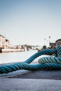 Close-up of rope against pier at harbor against clear sky