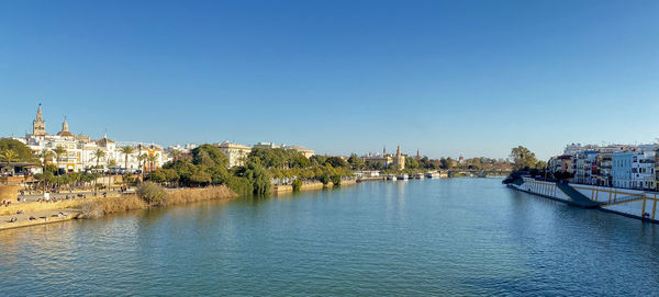 Panoramic view of river and buildings against clear blue sky