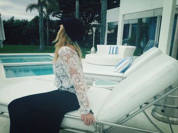 Young woman sitting on lounge chair at poolside in tourist resort