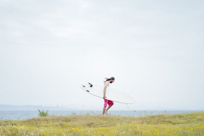 Man carrying surfboard while walking on meadow